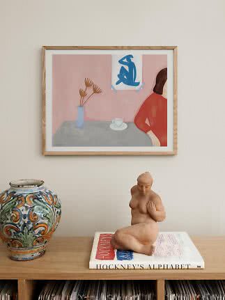 Stampa d’arte incorniciata sopra una credenza in legno con vaso, statuetta e libro
