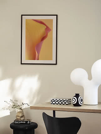 Indrammet blomsterplakat på beige væg over bord med sort-hvid vase og hvid skulpturlampe