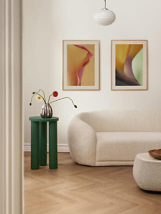 Stue med cremefarvet bouclésofa, grønt sidebord, vase med blomster og to indrammede kunsttryk