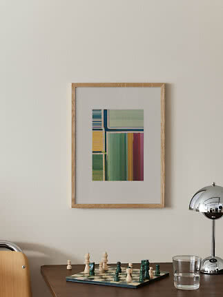 Inramad abstrakt poster med färgade ränder ovanför ett bord med schackbräde, lampa och glas