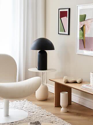 Sort bordlampe med kuppelformet skærm på rundt hvidt sidebord i moderne stue