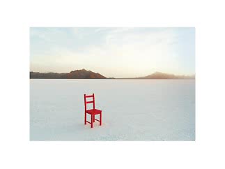 Roter Stuhl steht allein auf weißer Salzfläche, Berge am Horizont bei Sonnenuntergang