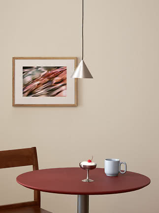 Tavolo rotondo rosso con tazza azzurra e piccolo dessert sotto lampada a sospensione argentata.