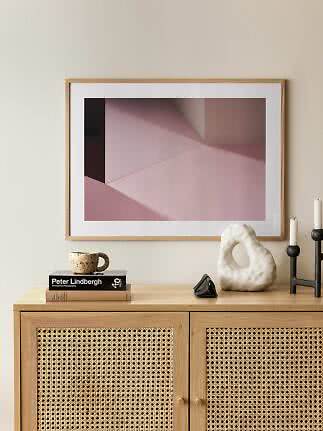 Stampa astratta geometrica rosa incorniciata sopra un mobile in legno chiaro con decori