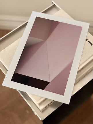 Stampa d’arte astratta incorniciata nei toni rosa e malva, appoggiata su libri
