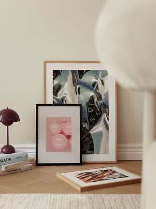 Framed art prints on the floor beside a purple table lamp and stacked books.