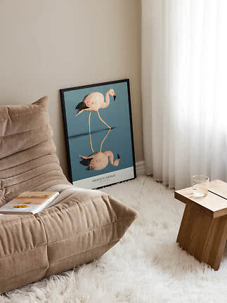 Poster incorniciato con fenicottero e riflesso, appoggiato al muro accanto a un divano beige
