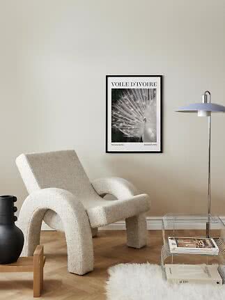 Framed white peacock poster on a beige wall above a cream boucle lounge chair
