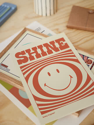 Poster SHINE con faccina sorridente su una scrivania con cornici e fogli