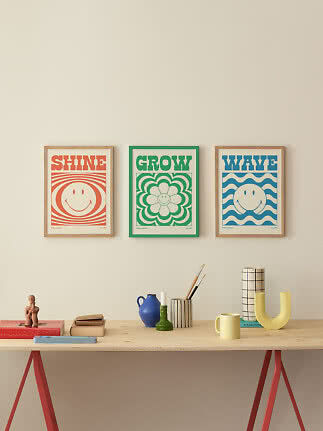 Three colorful framed smiley posters above a wooden table with decorative objects.