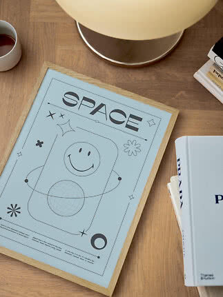 Lyseblå indrammet plakat med ordet SPACE på træbord ved lampe, bøger og kop