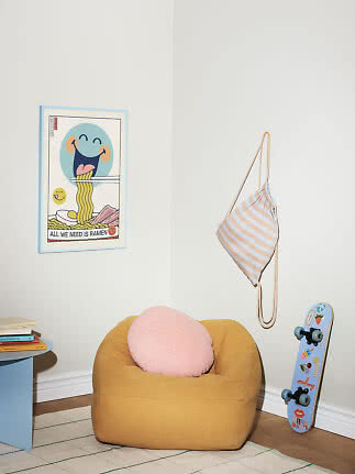Gestreifter Stoffbeutel hängt an der Wand über einem gelben Pouf im Kinderzimmer.