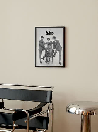 Framed black-and-white Beatles poster on a beige wall above a black chair and chrome side table