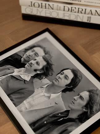 Framed black-and-white portrait of four men on a wooden floor beside a stack of books