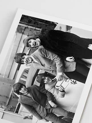 Black-and-white photo of four young people smiling beside a car