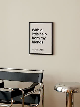 Indrammet typografiplakat med Beatles-citat på beige væg over sort stol og kromskammel