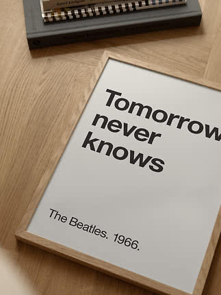 Affiche dans un cadre en bois clair avec « Tomorrow never knows » et « The Beatles. 1966. » sur parquet.