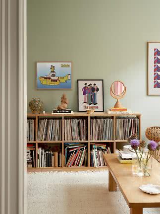 Wohnzimmer mit niedrigem Regal voller Schallplatten, gerahmten Postern und Holztisch mit lila Blumen