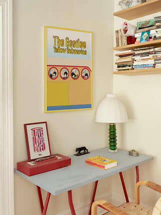 Inramad Beatles Yellow Submarine-affisch på ljus vägg ovanför grått bord med lampa och böcker
