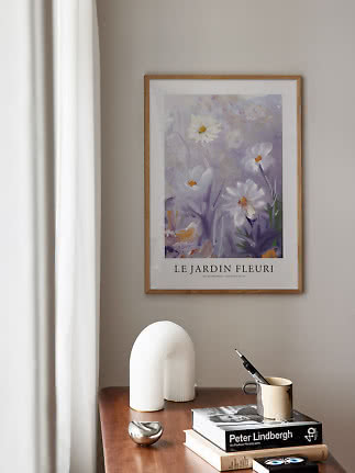 Inramad blomsteraffisch över träbord med böcker, mugg och vit skulptural lampa