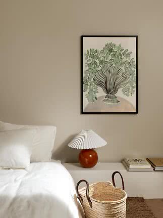 Bedroom with white bed, orange table lamp and framed botanical print on beige wall