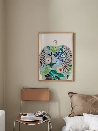 Indrammet farverig kunstplakat med kvinde og blomster over stol ved seng