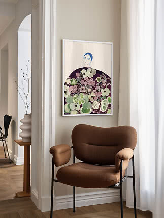 Indrammet kunsttryk af kvinde omgivet af blomster, hængt over brun lænestol i lyst hjørne