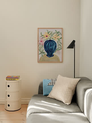 Living room corner with gray sofa, black floor lamp and framed floral print with blue vase on beige wall