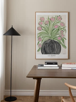 Ingelijste poster met roze tulpen in zwarte vaas boven een houten tafel naast een zwarte vloerlamp