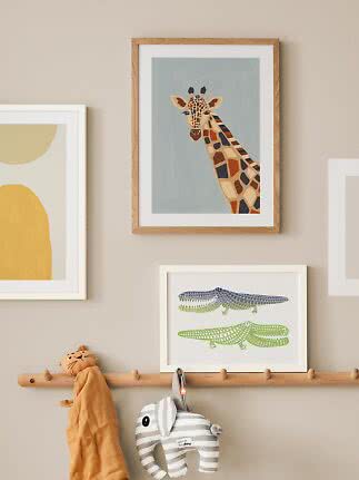 Kinderwanddeko mit gerahmtem Giraffenbild über einer Hakenleiste mit weichem Elefanten