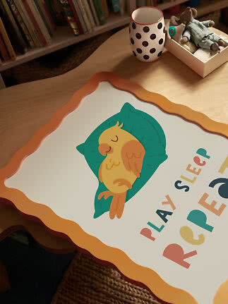 Børneplakat med sovende fugl på pude og teksten "Play Sleep Repeat" på et træbord