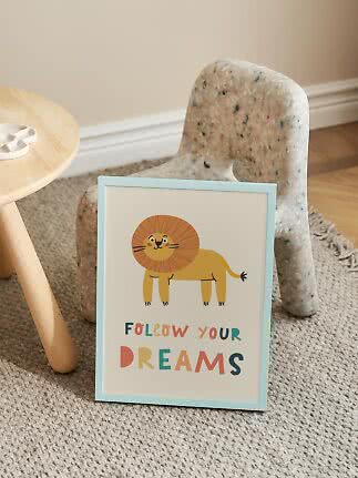 Poster per bambini incorniciato con leone e scritta "Follow Your Dreams" davanti a una sedia