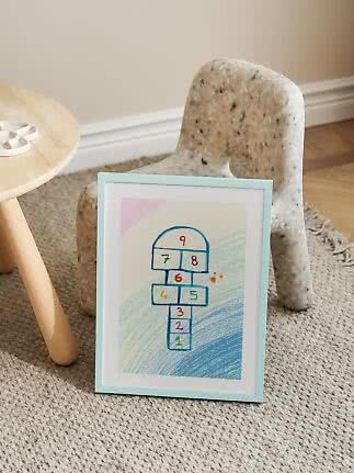 Framed hopscotch drawing with numbers, leaning against a speckled children's chair on a rug