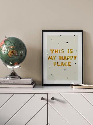 Framed "This is my happy place" print on a white cabinet beside a globe.