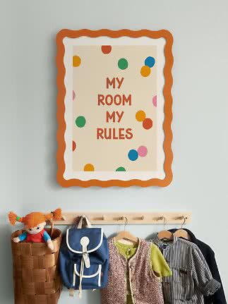 Children's poster reading "My Room My Rules" in an orange wavy frame above hooks with clothes and backpack