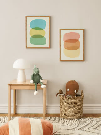 Children’s room with two abstract posters, table lamp, green doll and basket with octopus toy
