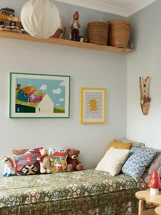 Cozy children's room with floral daybed, cushions, stuffed toys, wall art and baskets on a high shelf