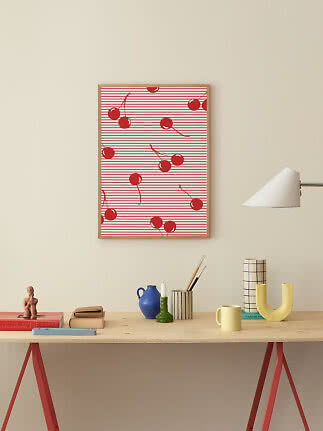 Lámina enmarcada con cerezas rojas sobre fondo de rayas, encima de una mesa de madera decorada