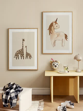 Barnrum med inramade posters av en giraff och en enhörning ovanför ett litet bord.