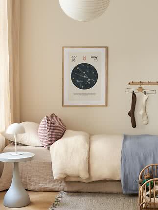 Hyggeligt børneværelse med Taurus-plakat over seng, hvid lampe og bløde puder