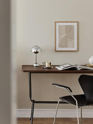 Minimalistischer Schreibtisch mit Chromlampe, Tasse, offenem Buch und gerahmter abstrakter Kunst