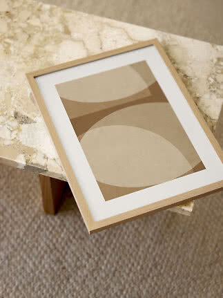 Abstract print in beige and brown tones in a light wood frame on a marble table