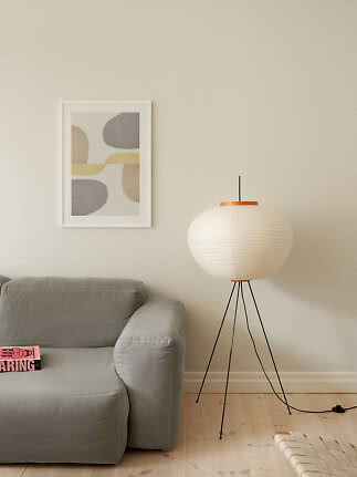 Wohnzimmer mit grauem Sofa, weißer Stehlampe auf Dreibein und abstraktem Wandbild