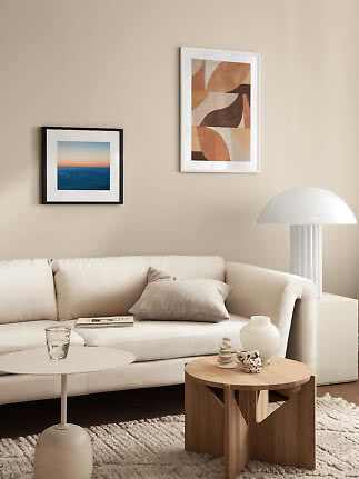 Helles Wohnzimmer mit beigem Sofa, Holztisch, weißer Lampe und zwei gerahmten Wandbildern