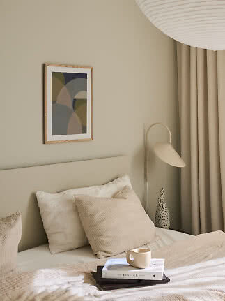 Camera da letto accogliente con letto neutro, cuscini, libro con tazza, lampada e arte astratta