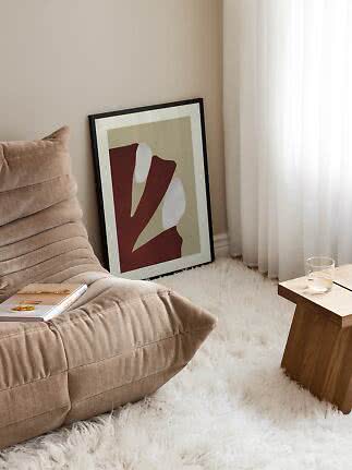 Abstrakter gerahmter Druck an der Wand neben beigem Sofa und weißen Vorhängen