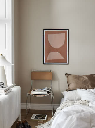 Minimalist bedroom with abstract wall art above a chair beside the bed