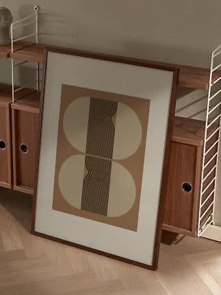 Framed abstract print with beige shapes and black wavy lines, leaning against a wooden shelving unit