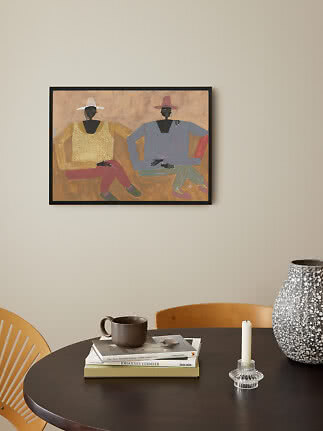 Framed painting of two seated figures wearing hats on a beige wall above a dark table