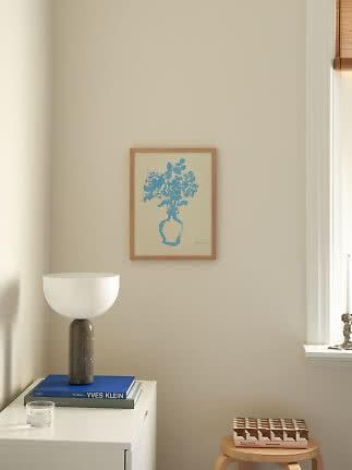 Framed blue floral print on beige wall above white cabinet with lamp and books